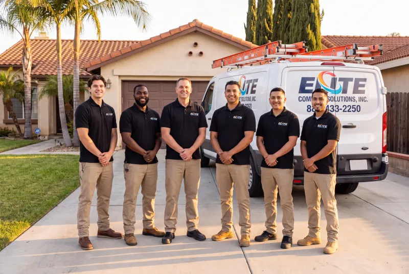 Six Elite Comfort Solutions technicians standing in a home's driveway in front of an Elite service van